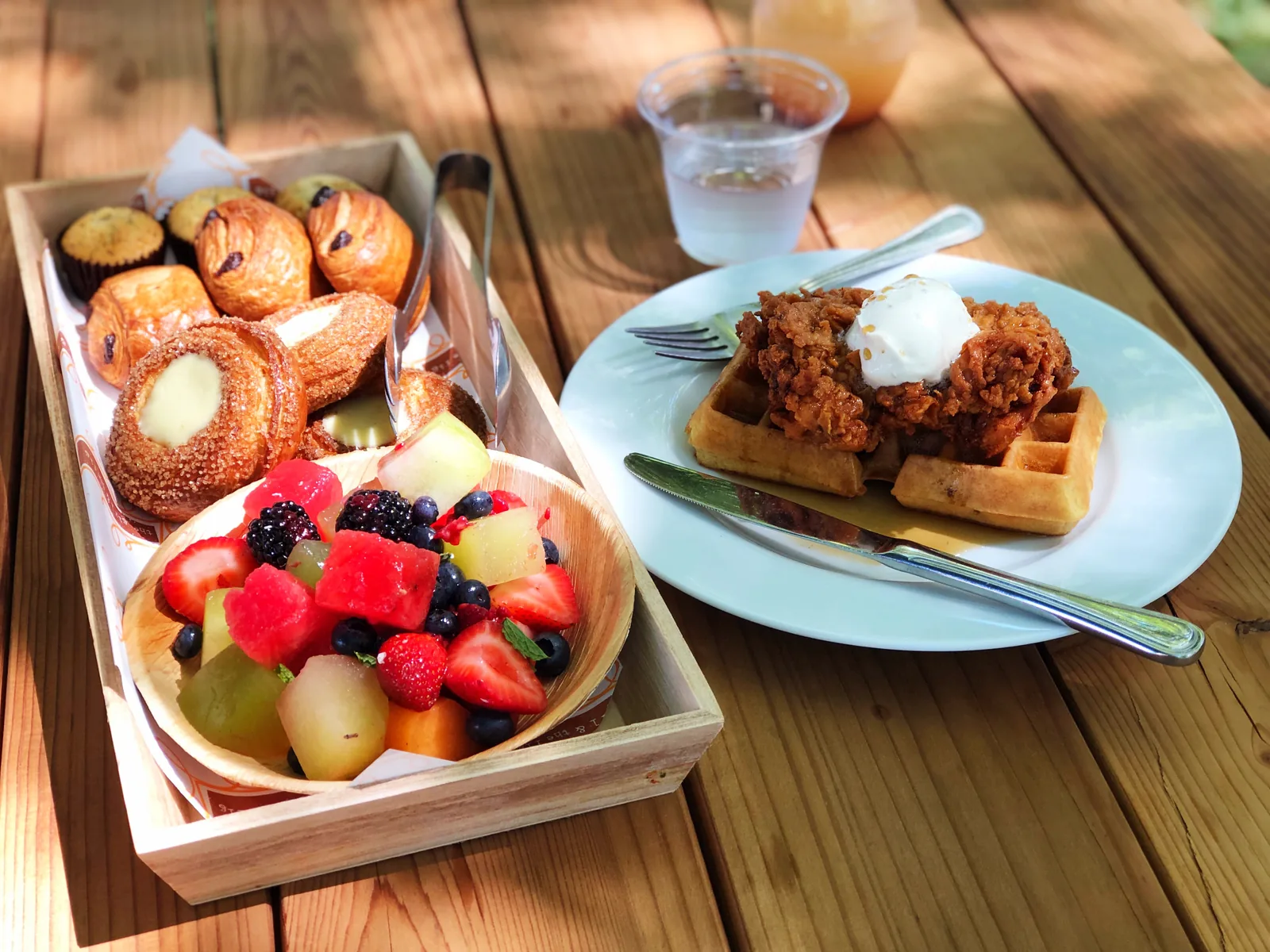A brunch spread of fresh fruit, pastries and chicken and waffles on a wooden table.