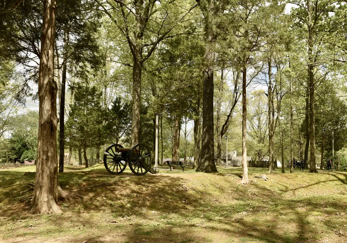 A reproduction cannon sits among tall trees on the earthworks of Fort Germantown, a Civil War redoubt preserved as a city park.