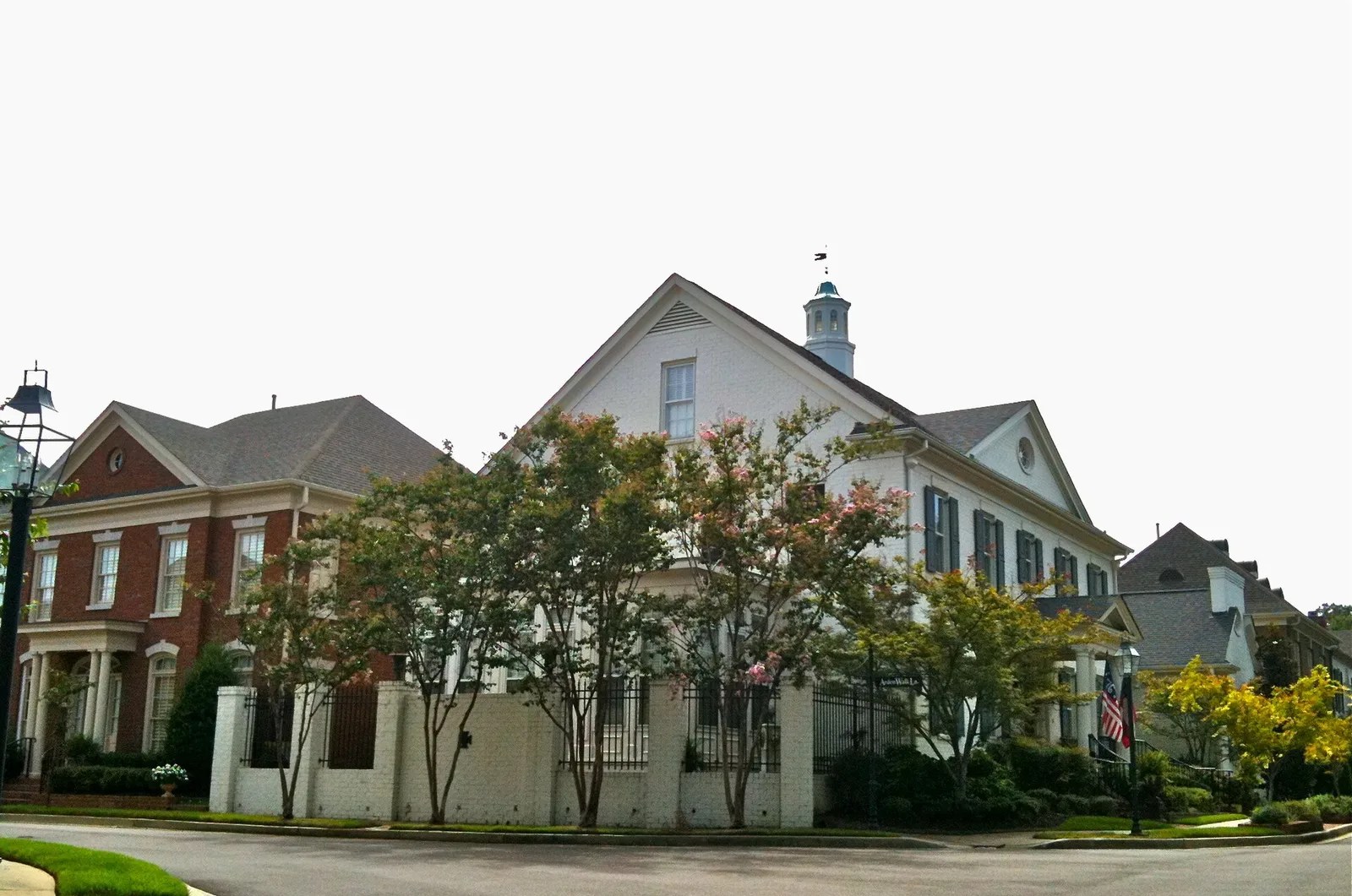 Two-story brick and white-painted houses behind a low wall and crape myrtles on a corner in Germantown.
