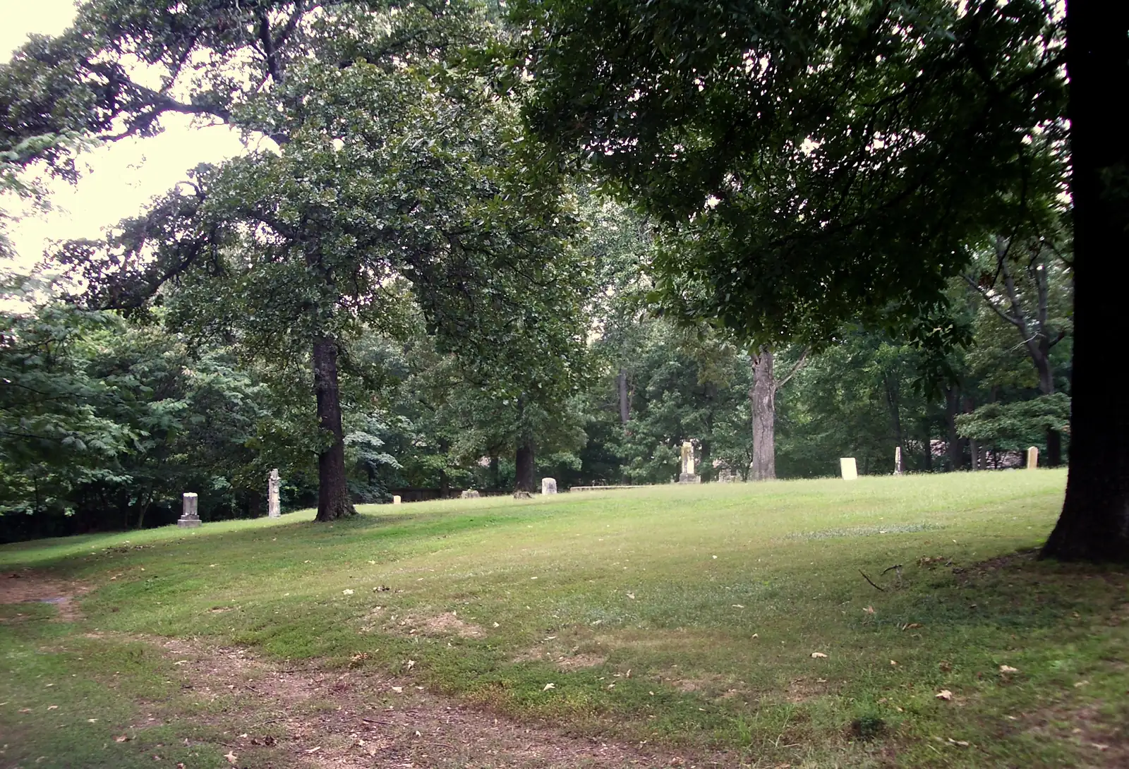 Old headstones stand on a shaded lawn under tall trees at Germantown Cemetery.